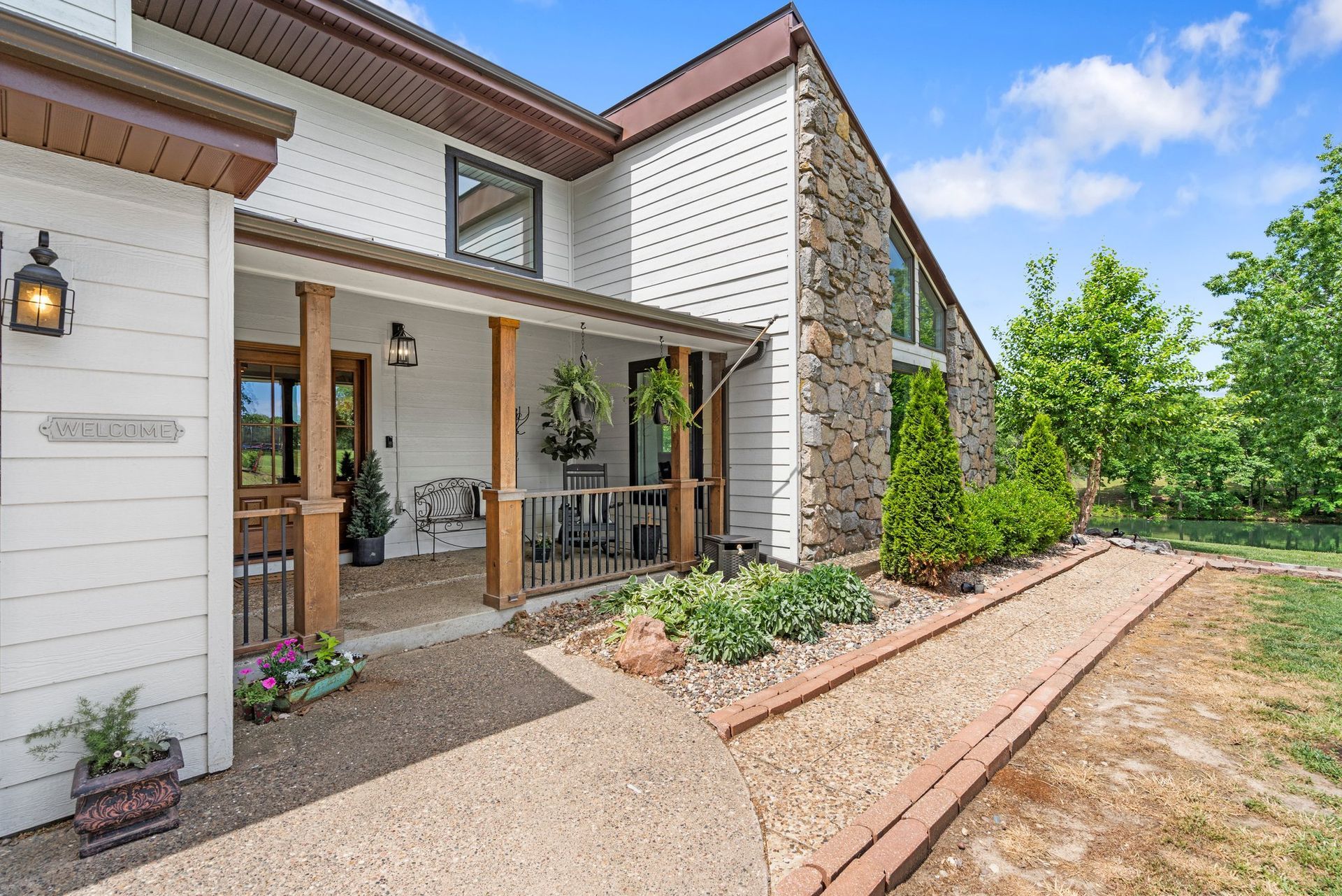 Two-story house with a stone facade and porch, gravel walkway, and a sunny sky.