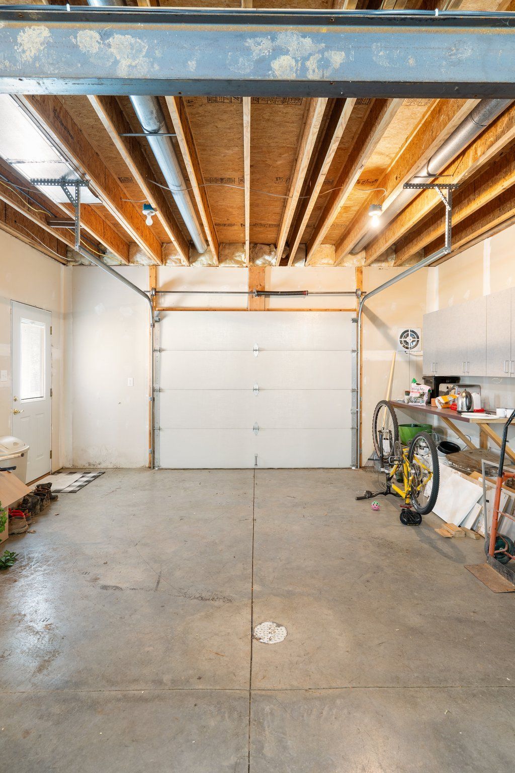 Garage interior with a closed white garage door, concrete floor, and exposed ceiling beams.