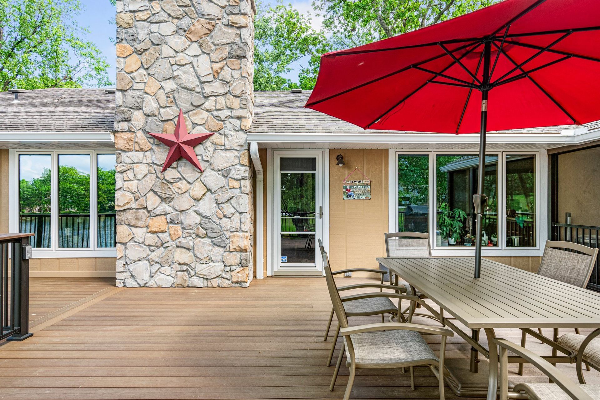 Outdoor patio with red umbrella, dining table, chairs, and stone chimney with star.