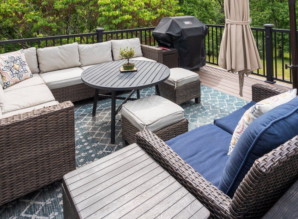 Outdoor deck with sectional sofa, round table, and grill. Blue and beige color scheme.