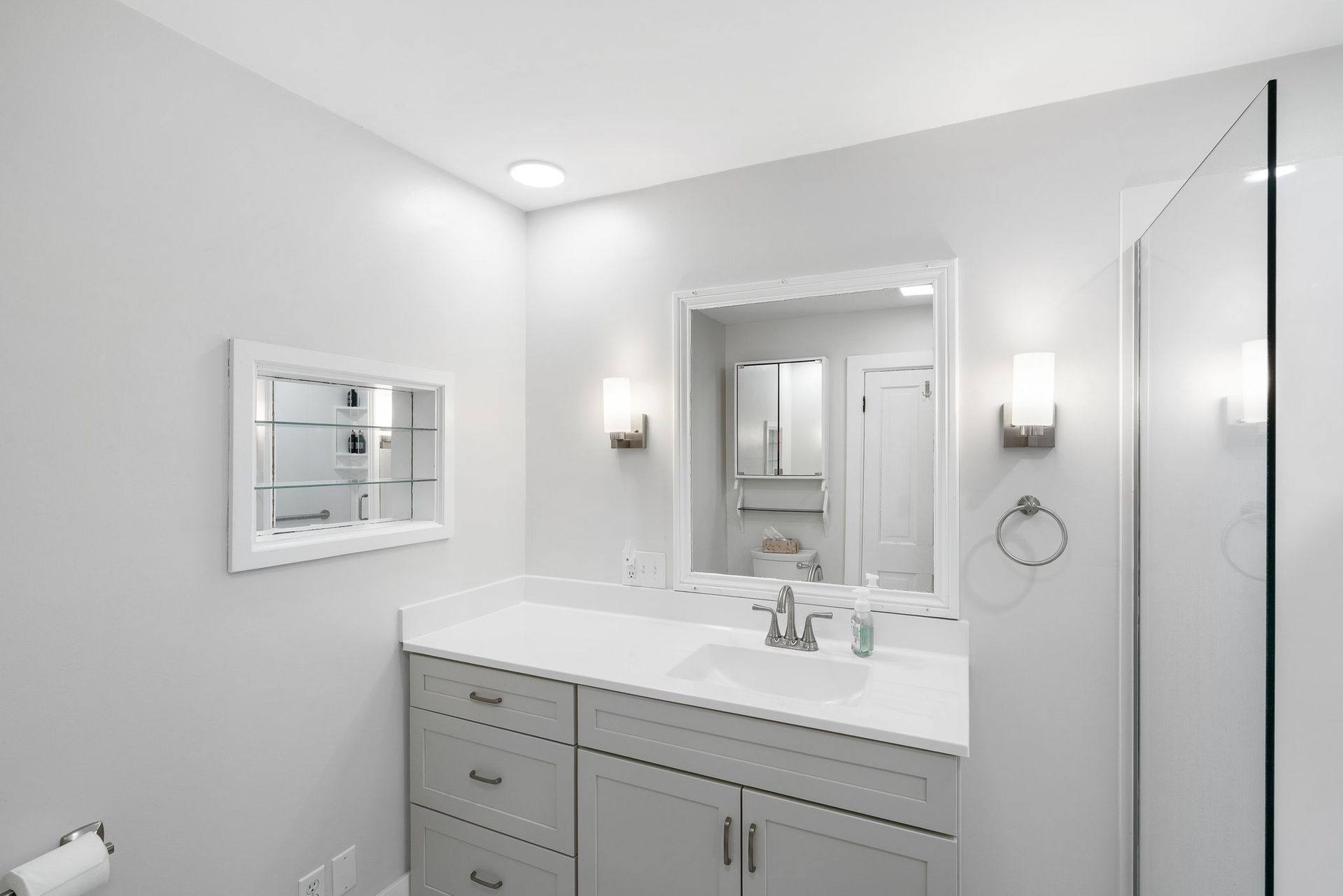 Bathroom with a gray vanity, white countertop, and a built-in medicine cabinet. White walls and a shower.