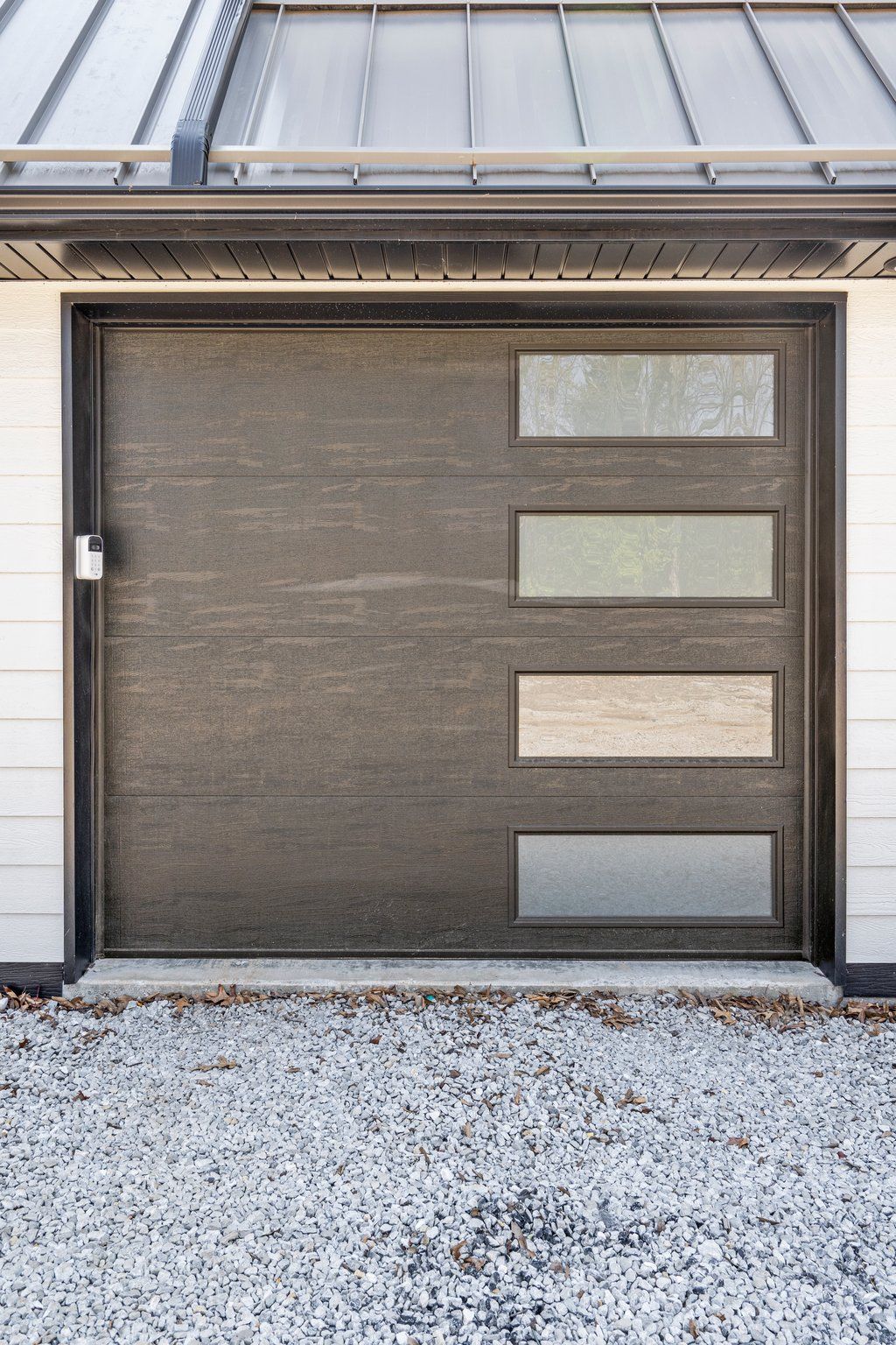 A wood-toned garage doors with windows and a metal roof above.