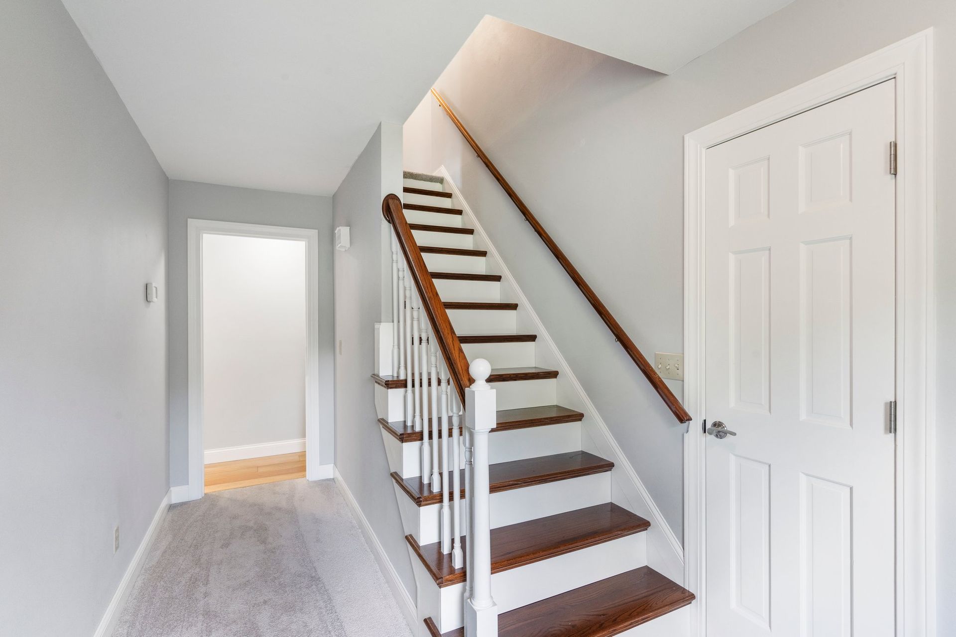 Hallway with staircase and white door; grey walls, wood steps, and brown handrails.
