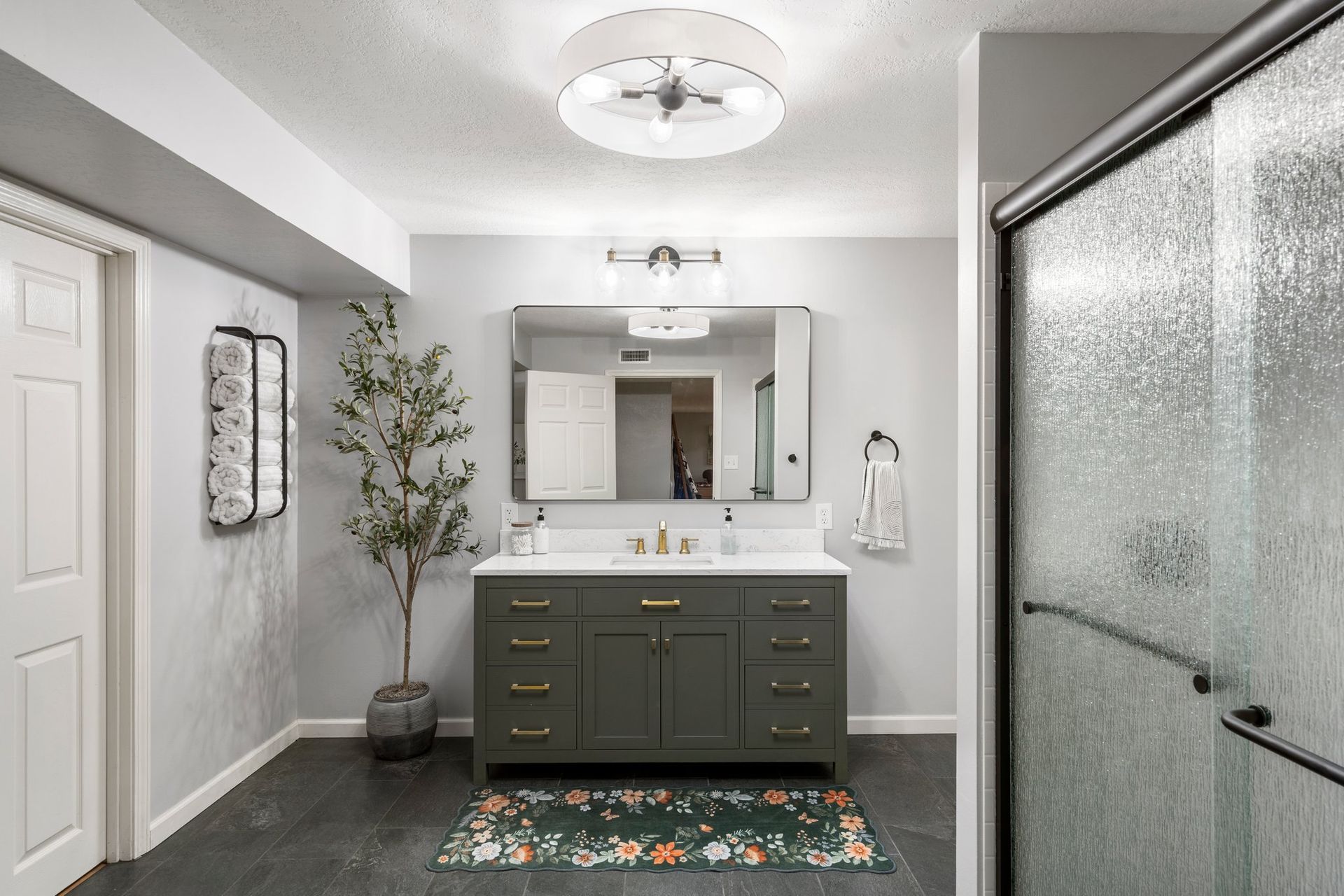 Bathroom with green vanity, large mirror, shower, and decorative rug.