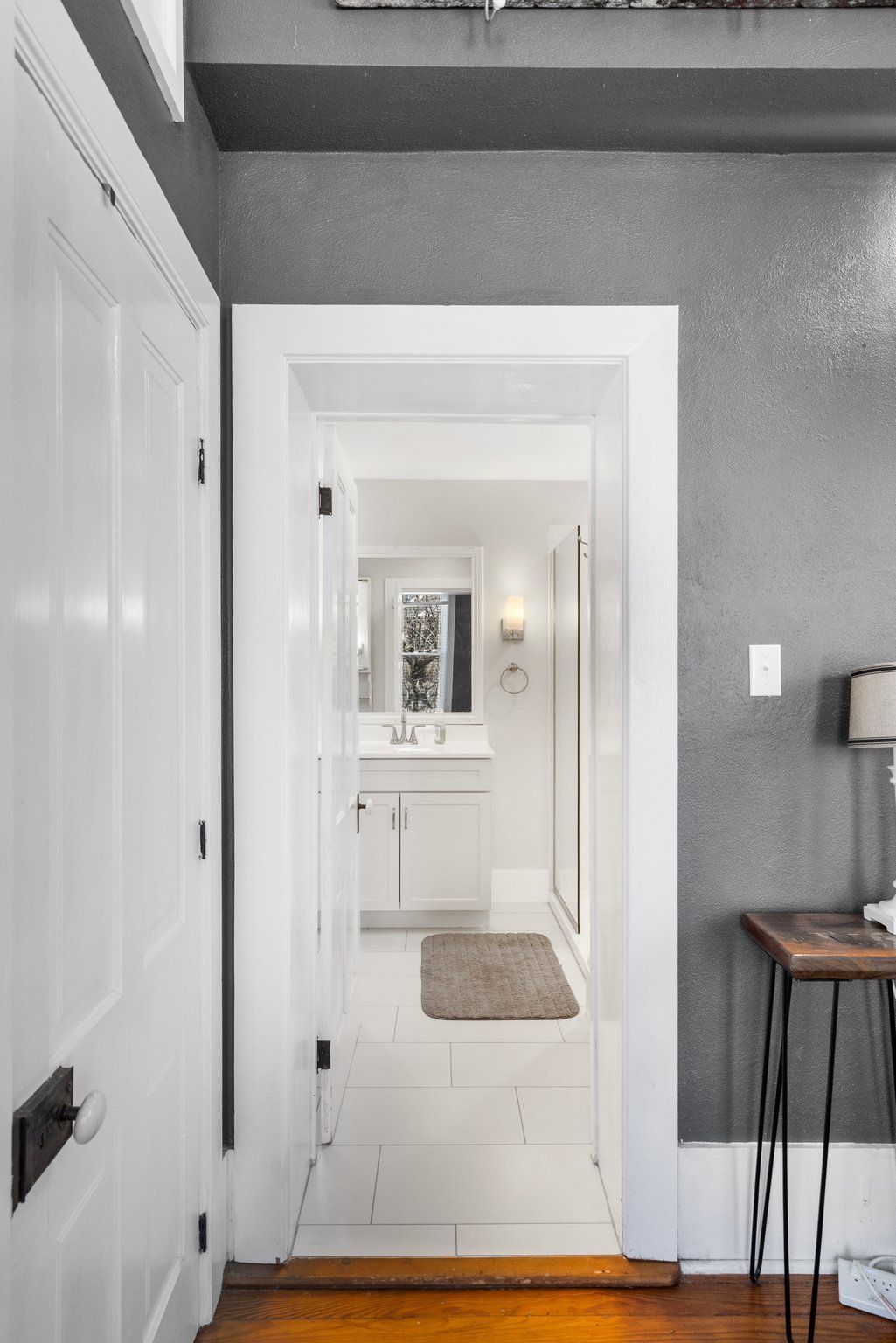 Doorway to a white bathroom with vanity, shower, and gray walls.