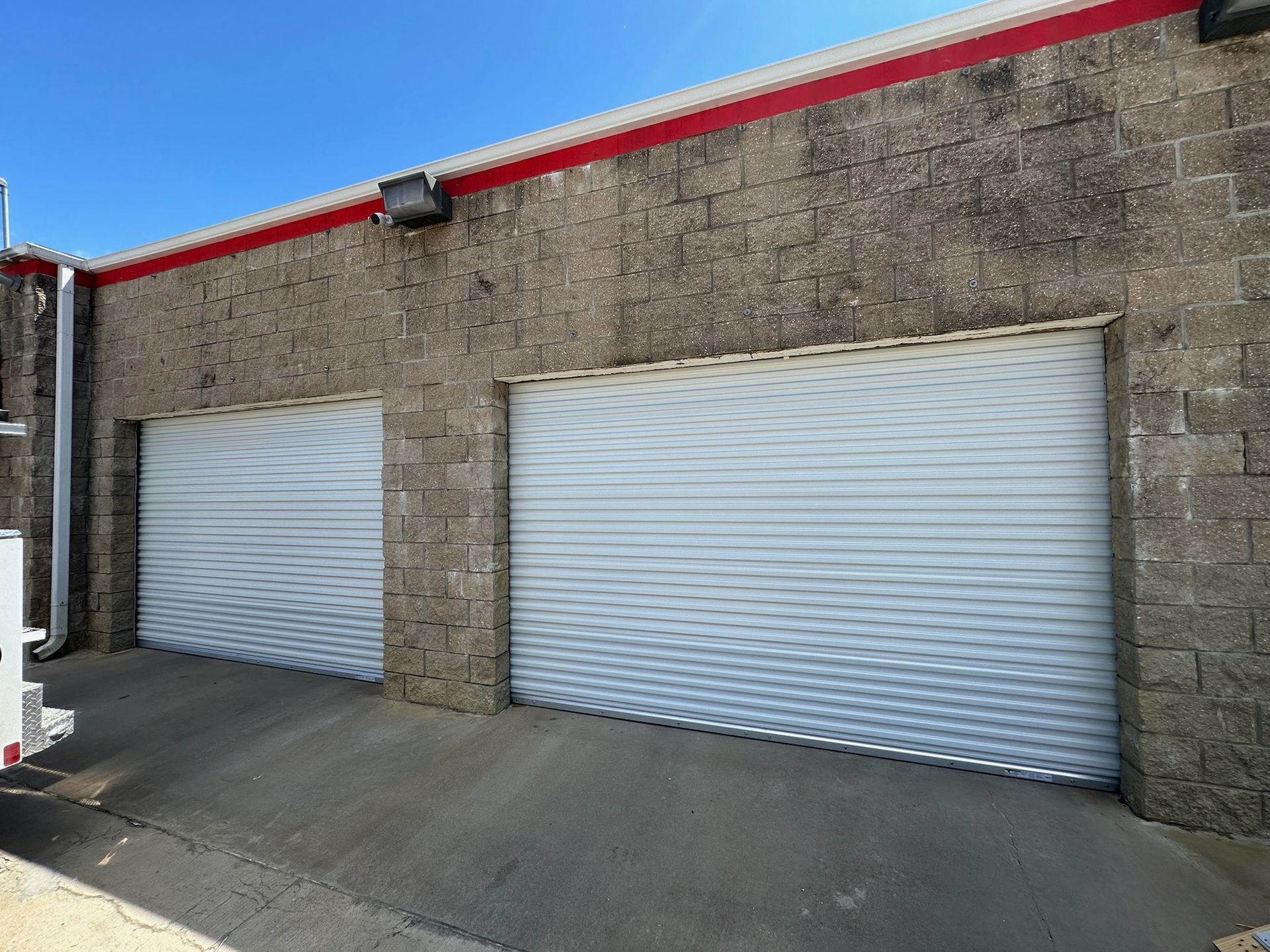 Two closed, white roll-up garage doors on a cinder block building. Red trim accents the roof.