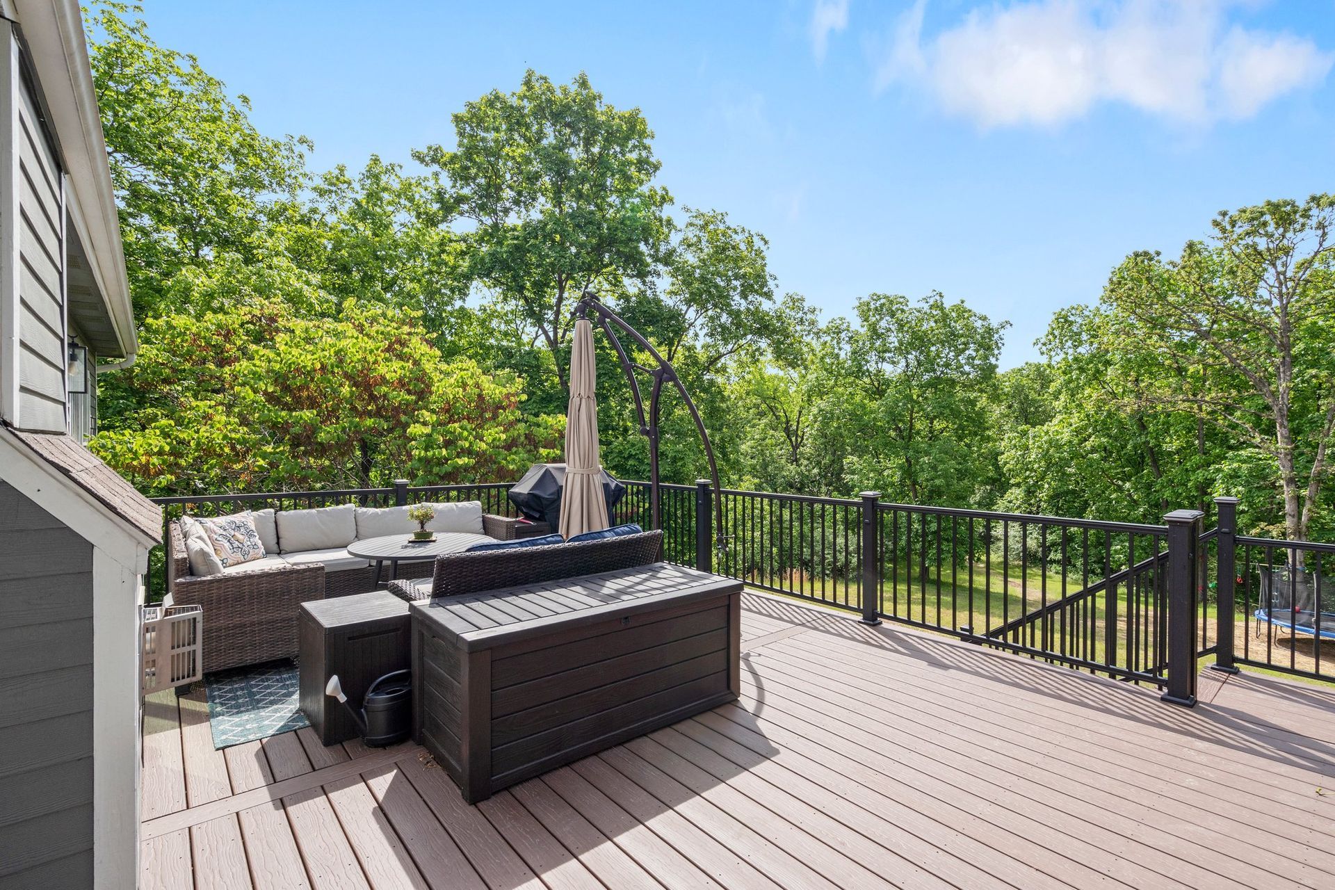 Wooden deck with outdoor furniture overlooking a wooded area. Blue sky with clouds.