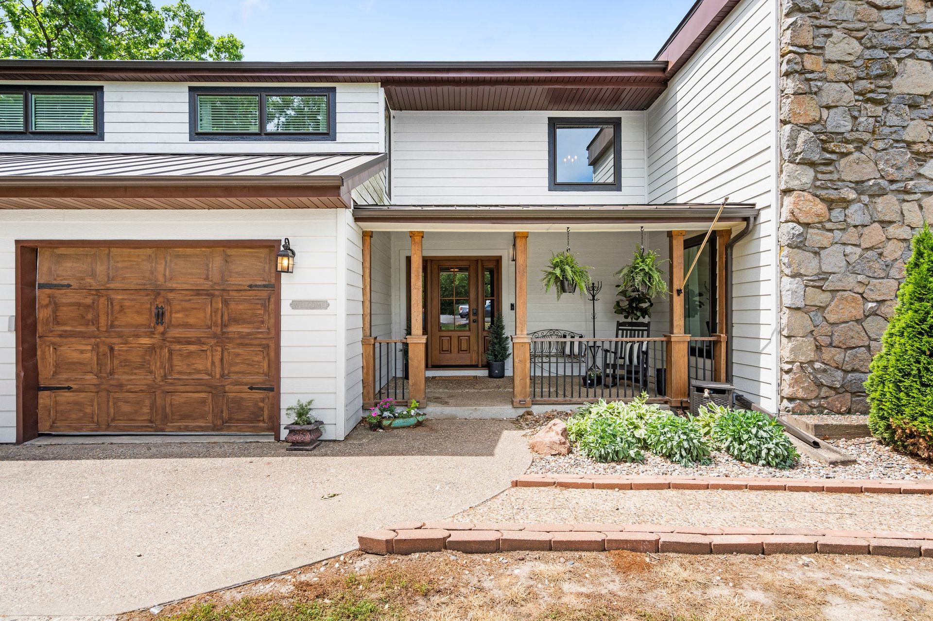 Two-story house with brown garage door, front porch, and stone chimney. Landscaping in front.