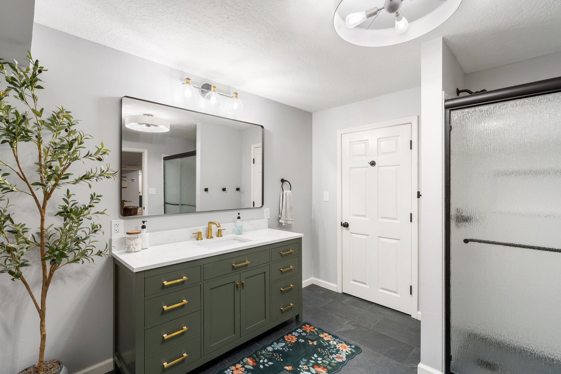 Bathroom with green vanity, large mirror, and glass shower door; gray walls.
