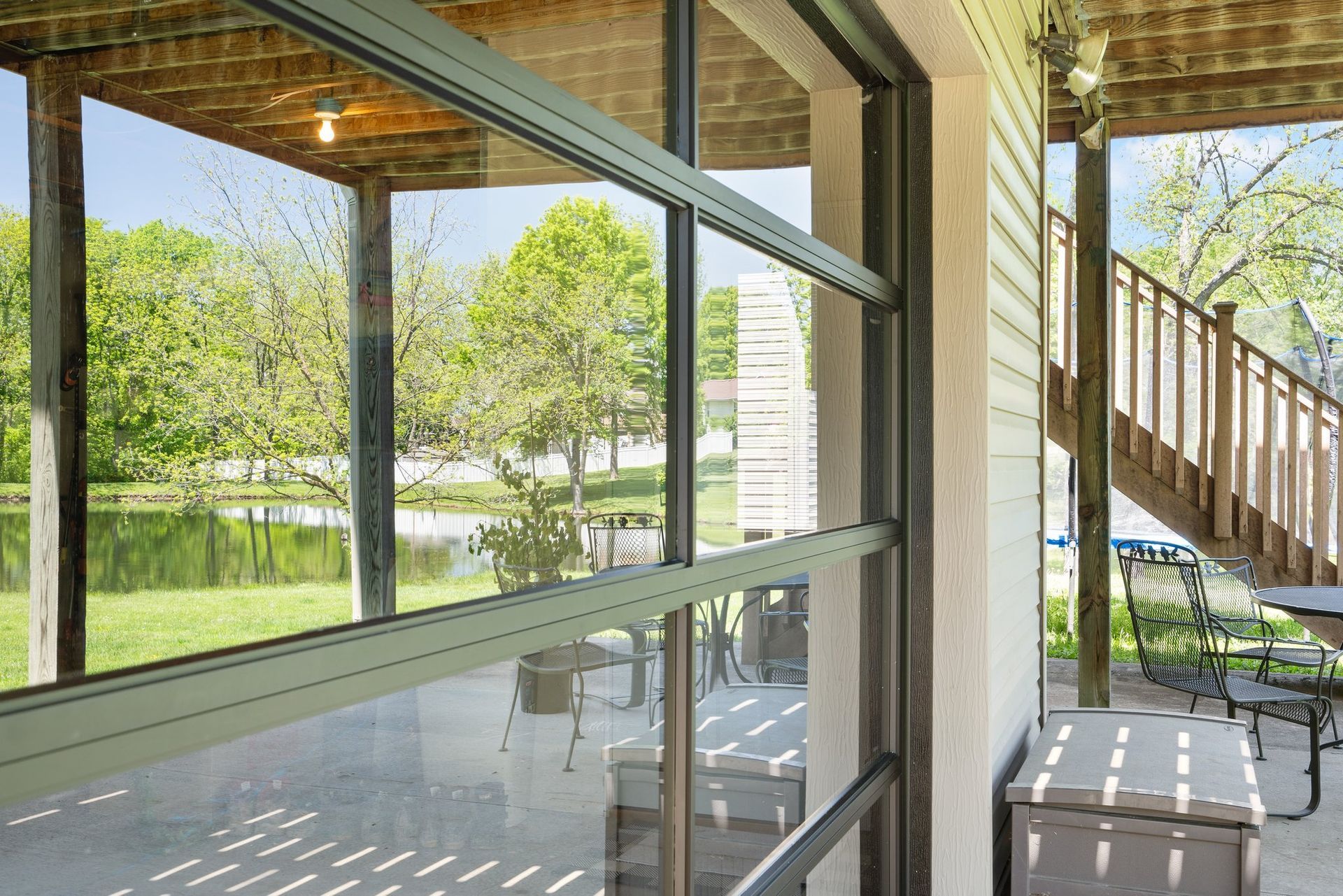 Glass door leading to a patio with lake view. Green trees, wooden deck, and outdoor furniture visible.