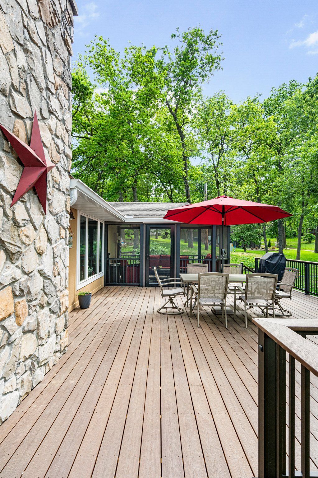 Wooden deck with outdoor seating under a red umbrella, next to a stone wall with a red star decoration.