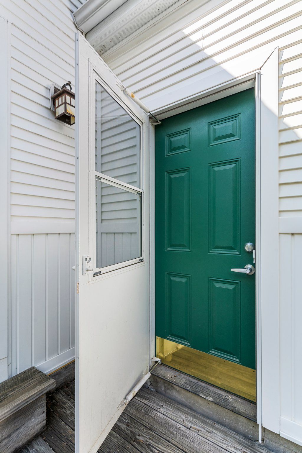 White screen door open, revealing a green door. Exterior shot, porch with white siding.
