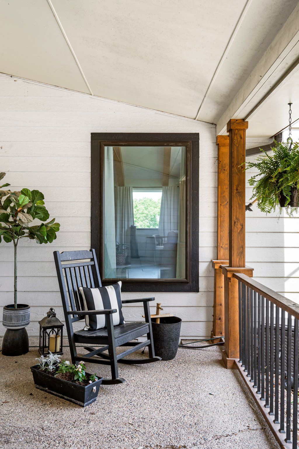 Covered porch with black rocking chair, large mirror, plants, and black railing.