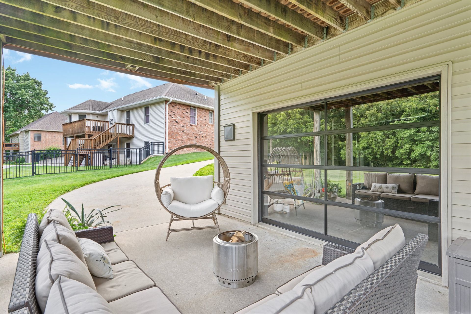 Covered patio with seating, fire pit, and glass door overlooking a yard.