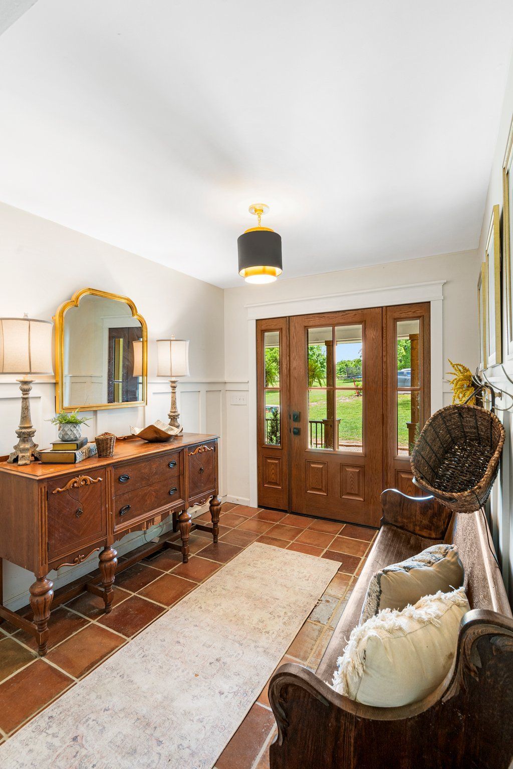 Entryway with wood doors, terracotta tile, antique furniture, and a rug.