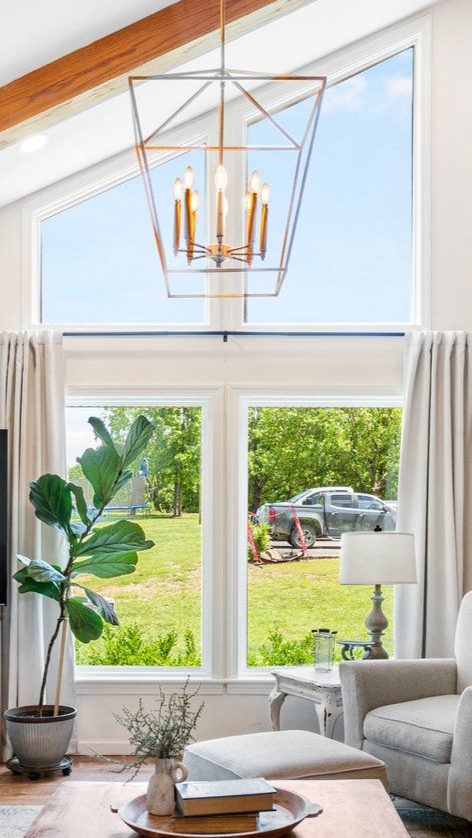 Living room with large windows, chandelier, beige curtains, and outdoor view of lawn and car.