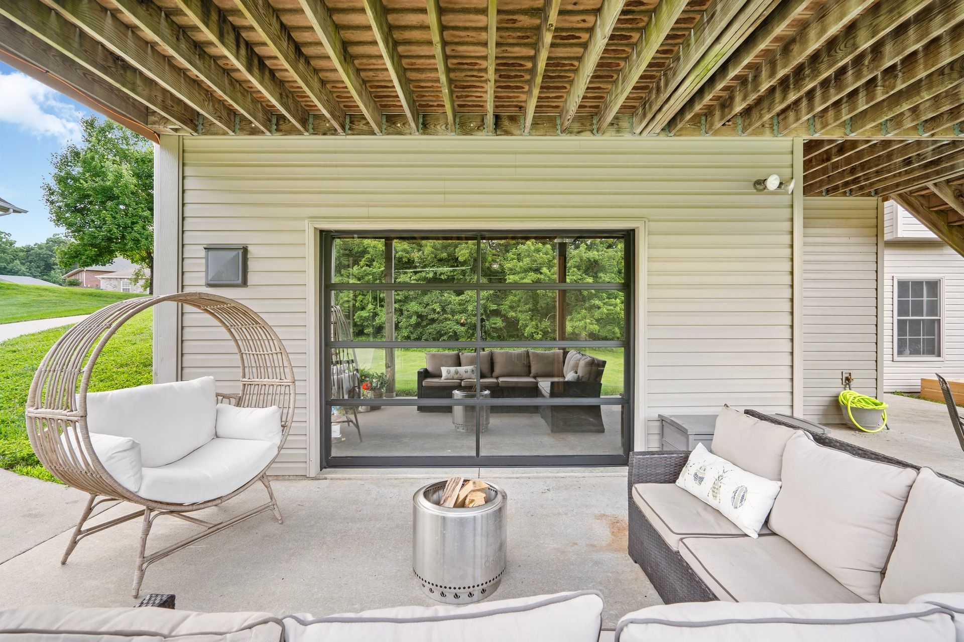 Outdoor patio with seating: swing chair, sofa, fire pit, and a glass garage door leading inside.