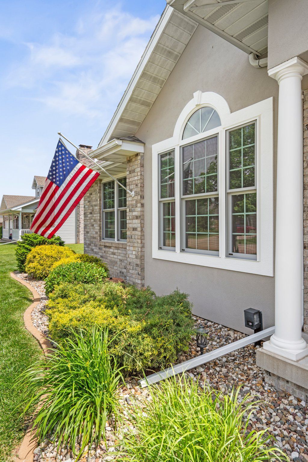 House exterior with American flag and window with arched top; landscaping in front.
