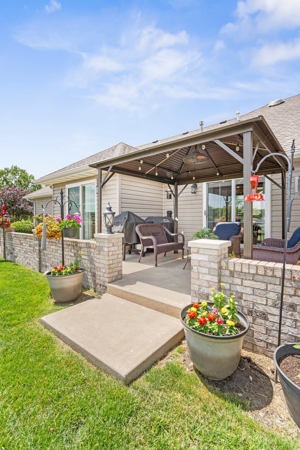 Patio with brick pillars, gray concrete, and a brown pergola with seating and potted flowers.