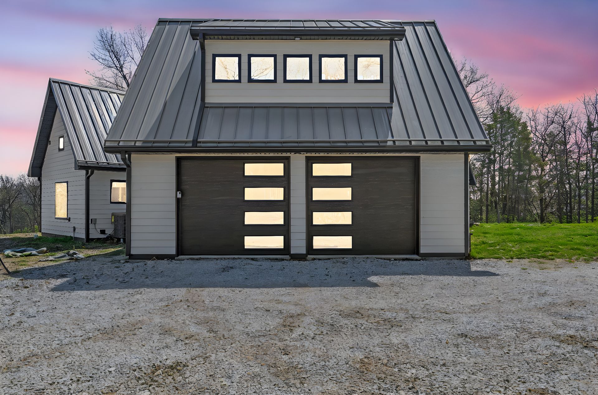Modern two-car garage with black metal roof, white siding, and windows. Gravel driveway.