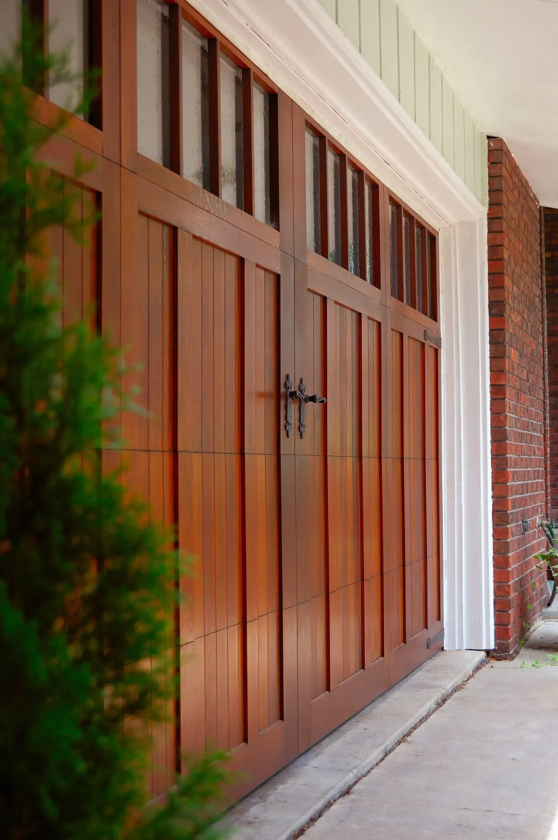 Wooden garage door with rectangular windows, brick wall, and concrete driveway.