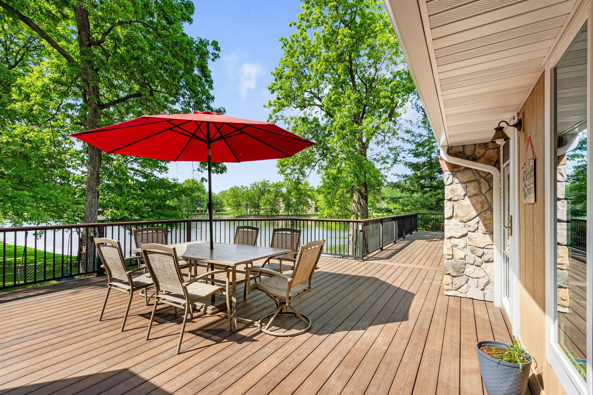 Deck with table and chairs, red umbrella, overlooking a lake.