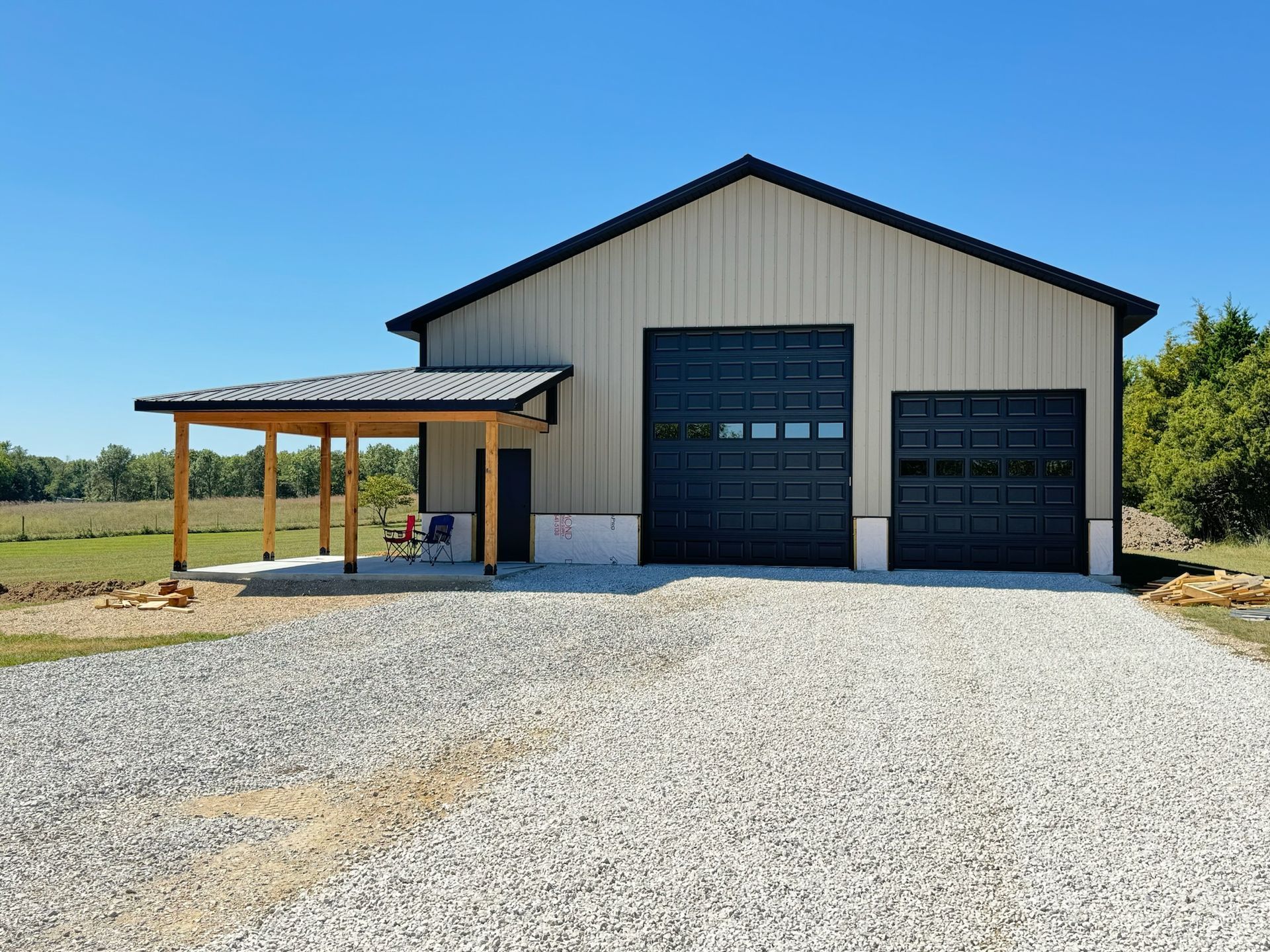Beige metal building with black garage doors and a gravel driveway.