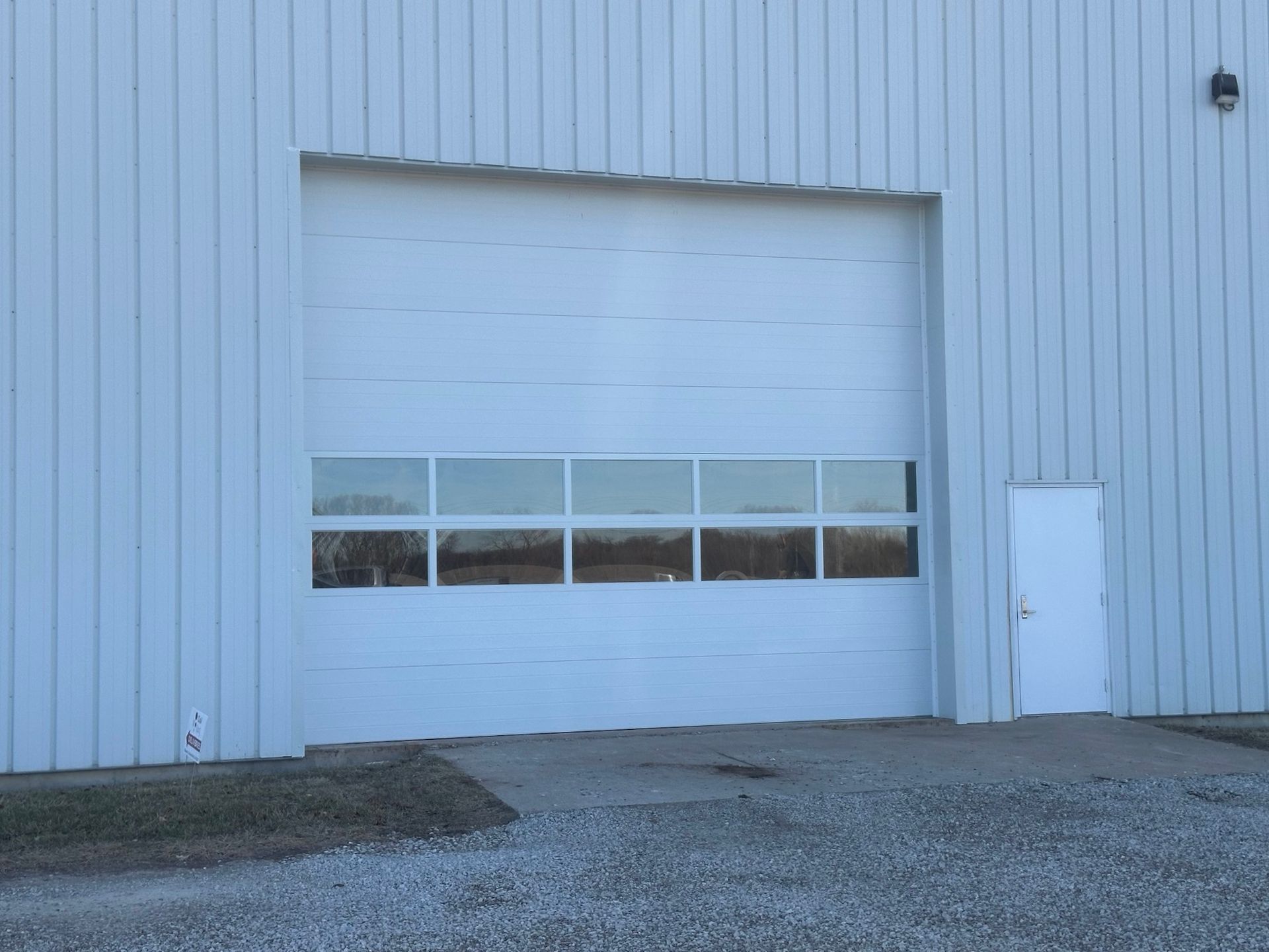 White warehouse with large closed garage door and a smaller door to the right.