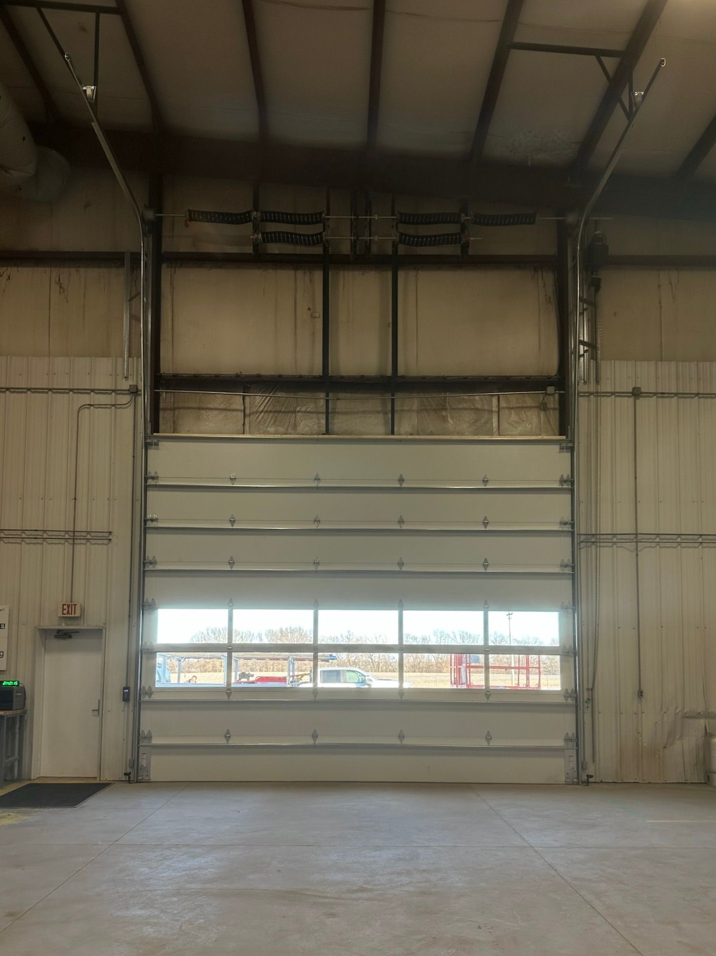 Interior view of an industrial building with a partially open, overhead garage door with a window.