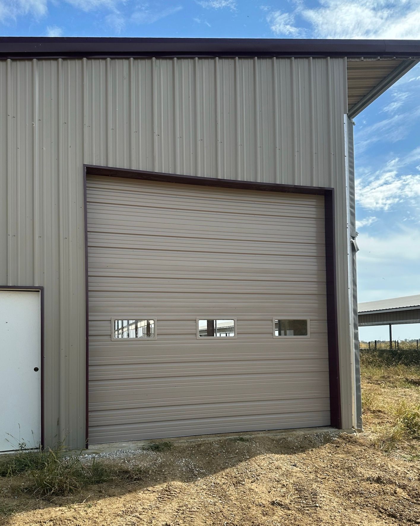 Tan metal garage door on a tan metal building with three small window panels; outdoor setting.