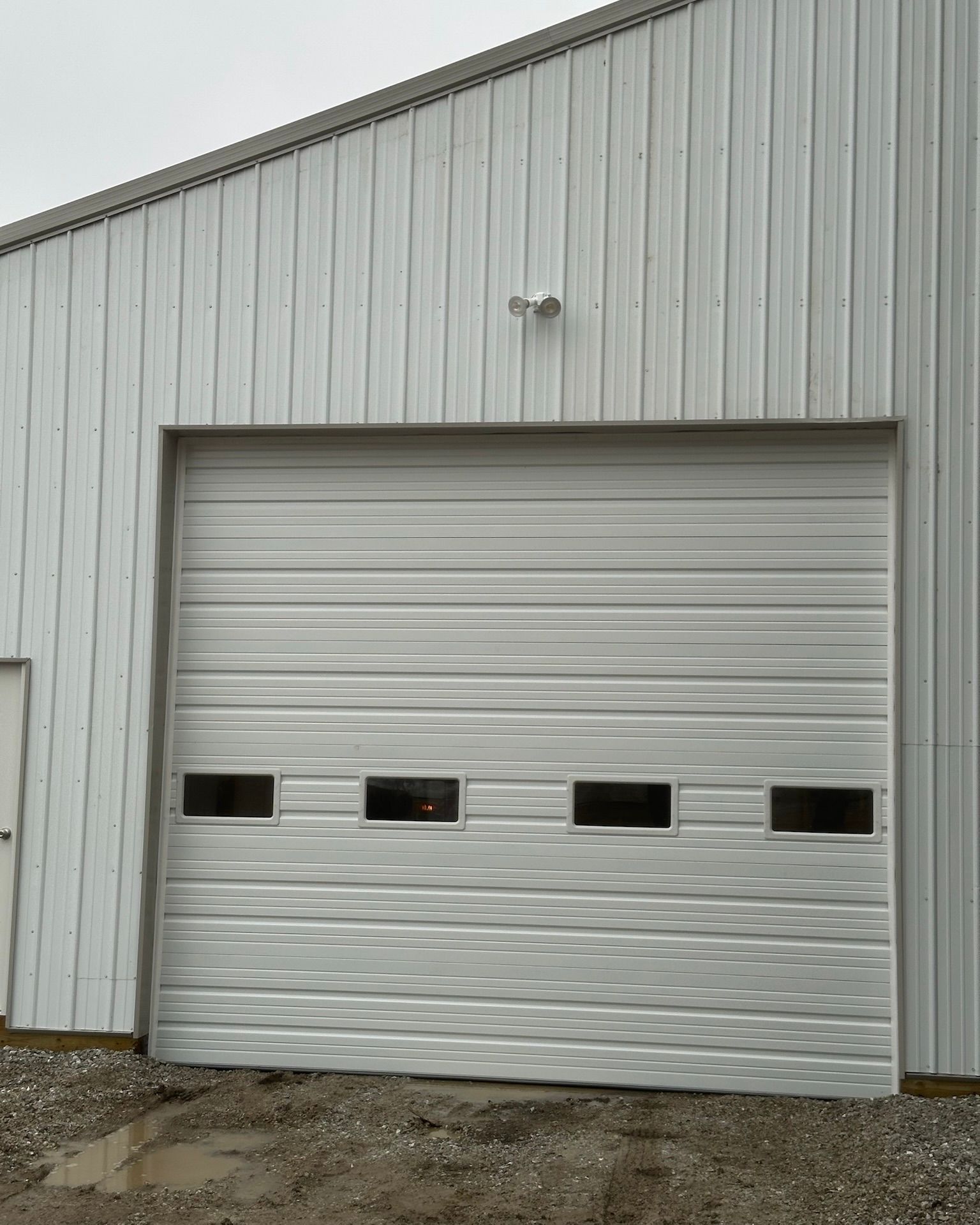 White metal garage door on a white metal building with small windows and a light above.