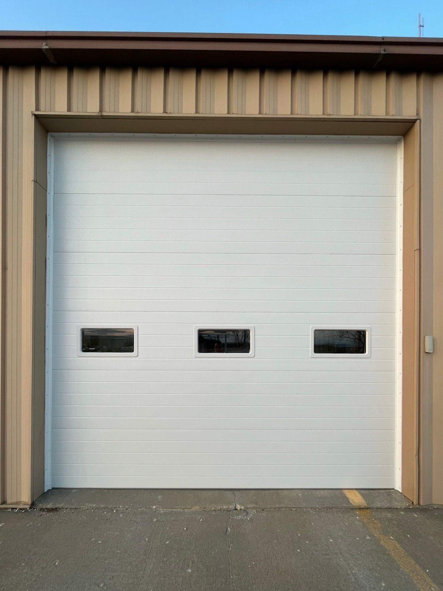White garage door with three small windows, on a tan building.