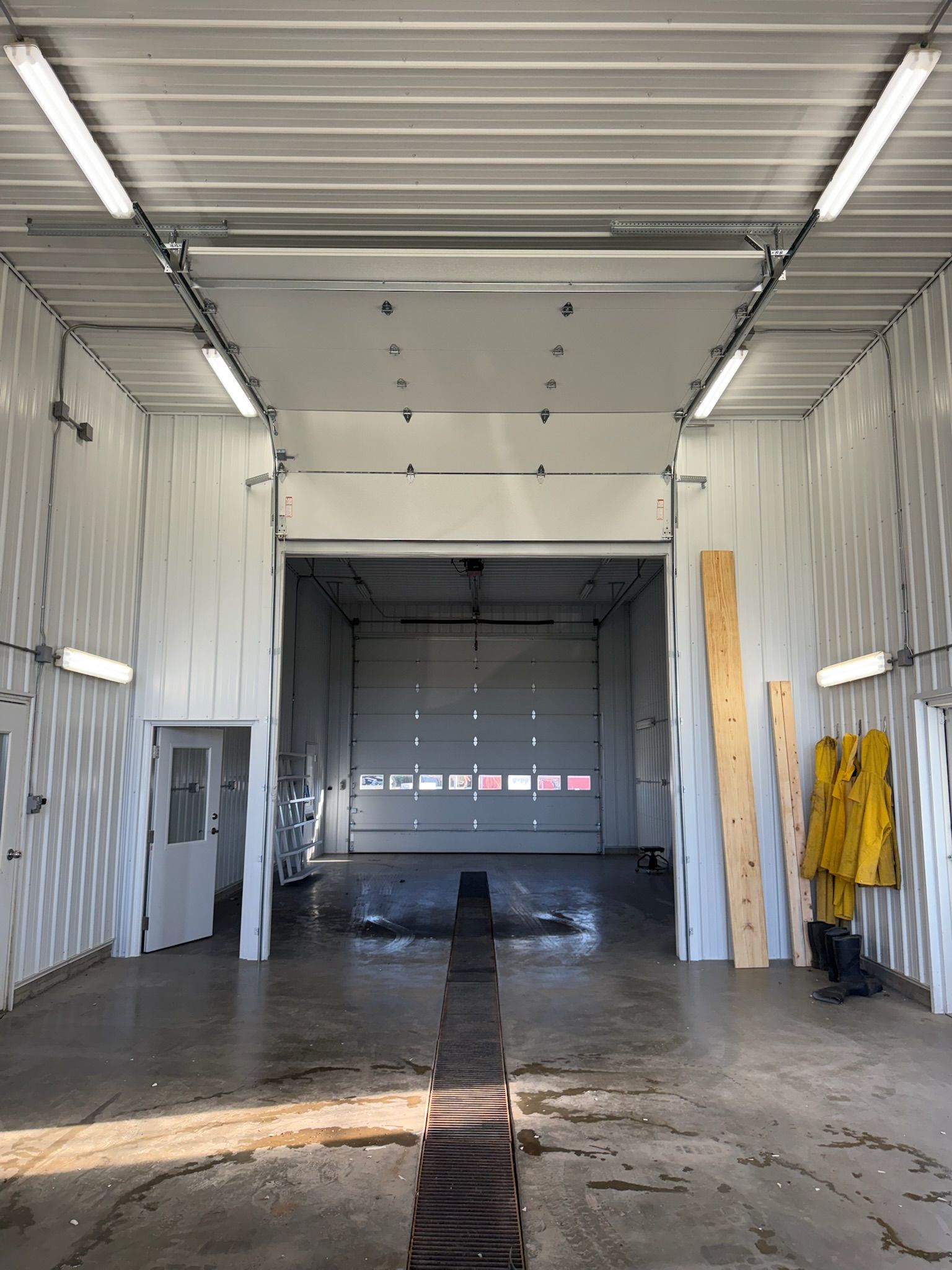 Interior of a garage or car wash bay with open bay doors; white walls and ceiling; concrete floor.