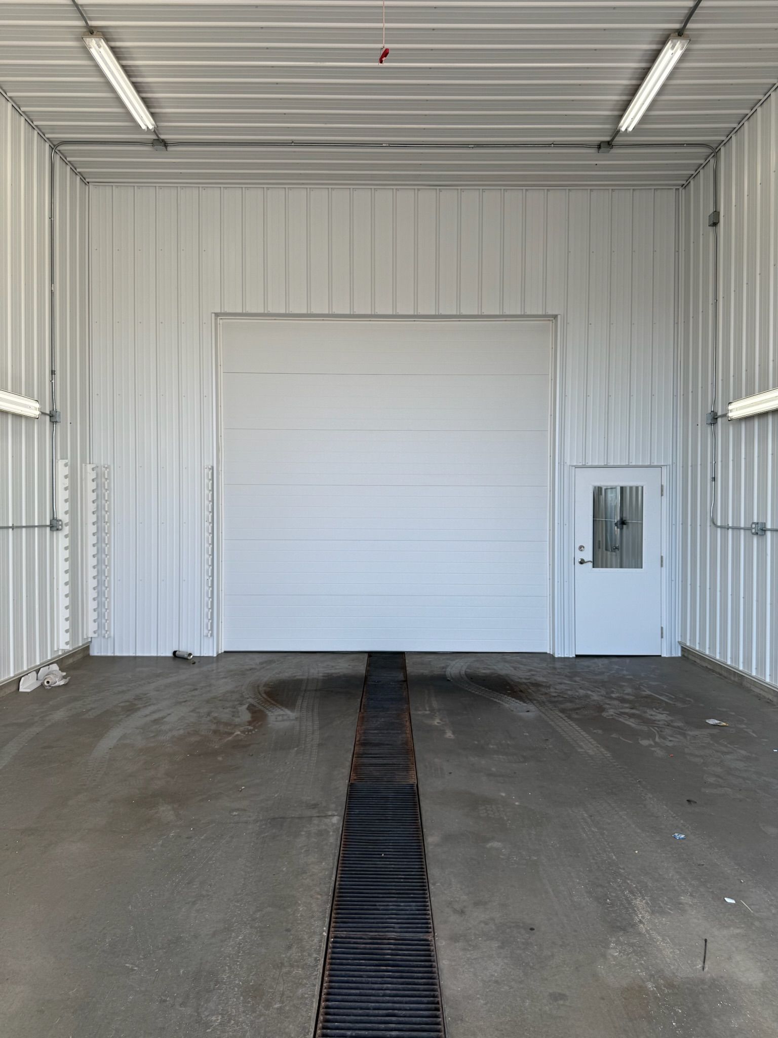 White interior of a garage, featuring a closed overhead door, a small door, and drainage on the floor.