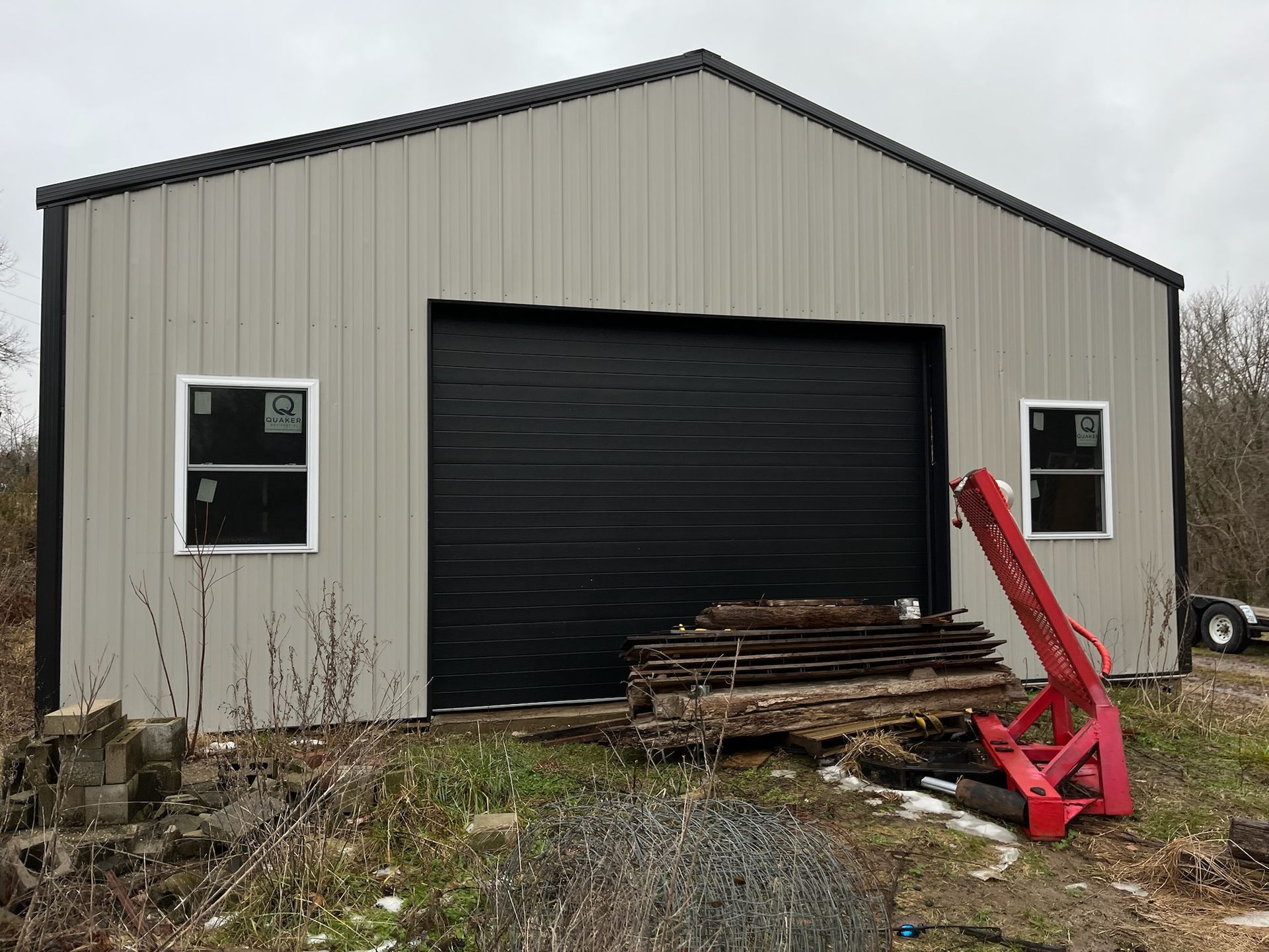 Metal building with black garage door, windows, and red lift. Gray siding, neutral setting.