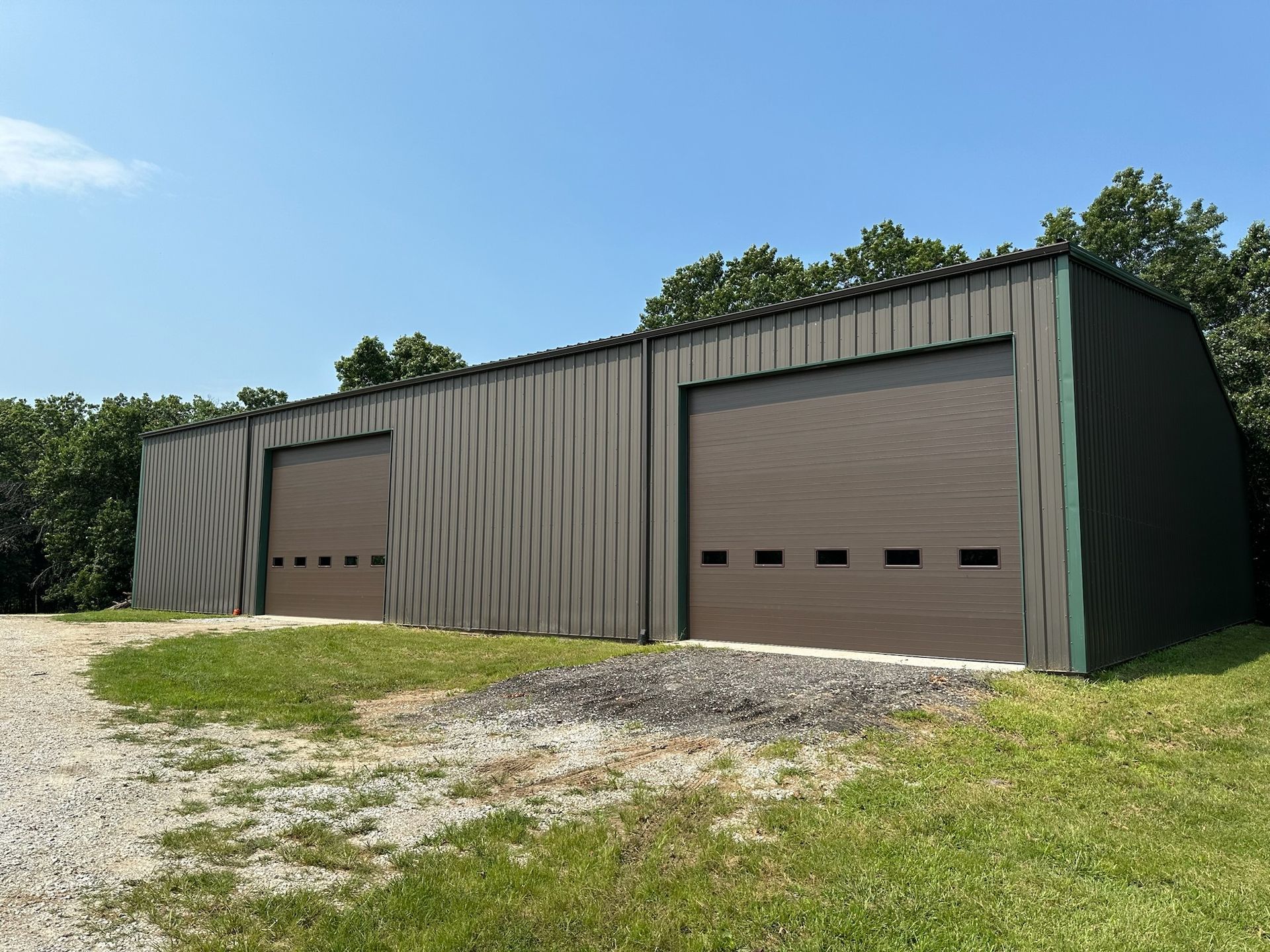 A metal building with two garage doors, set against a blue sky, on a gravel drive.