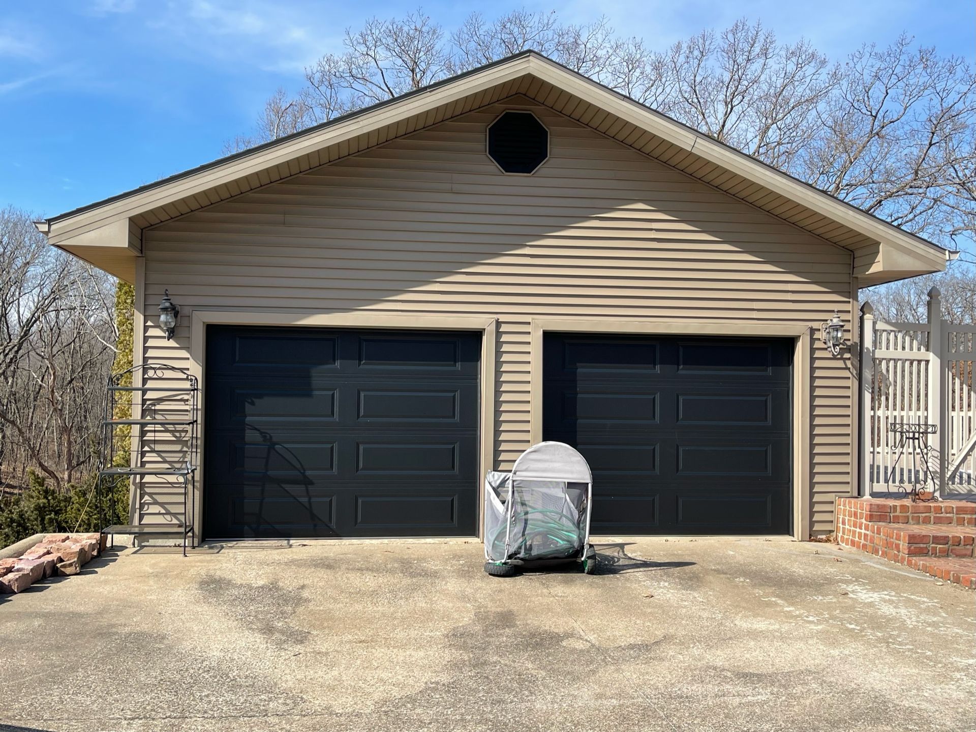 Tan two-car garage with black doors; grill covered in gray; blue sky background.