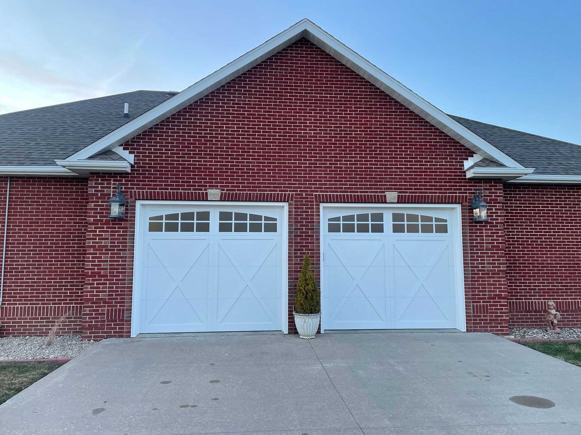 White garage doors on a brick building with a driveway, under a clear sky.