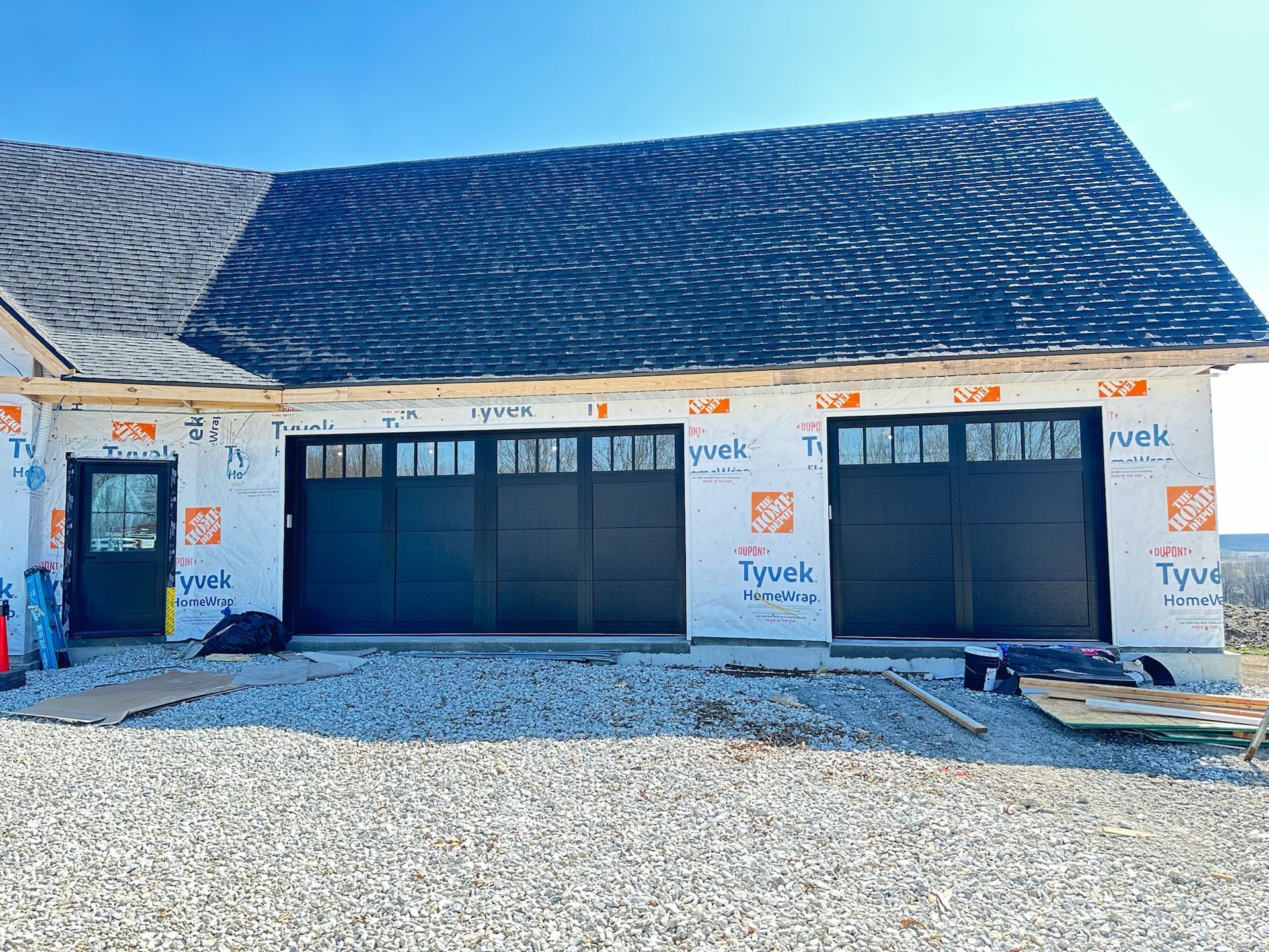 New garage with dark doors and roof, under construction, covered in Tyvek.