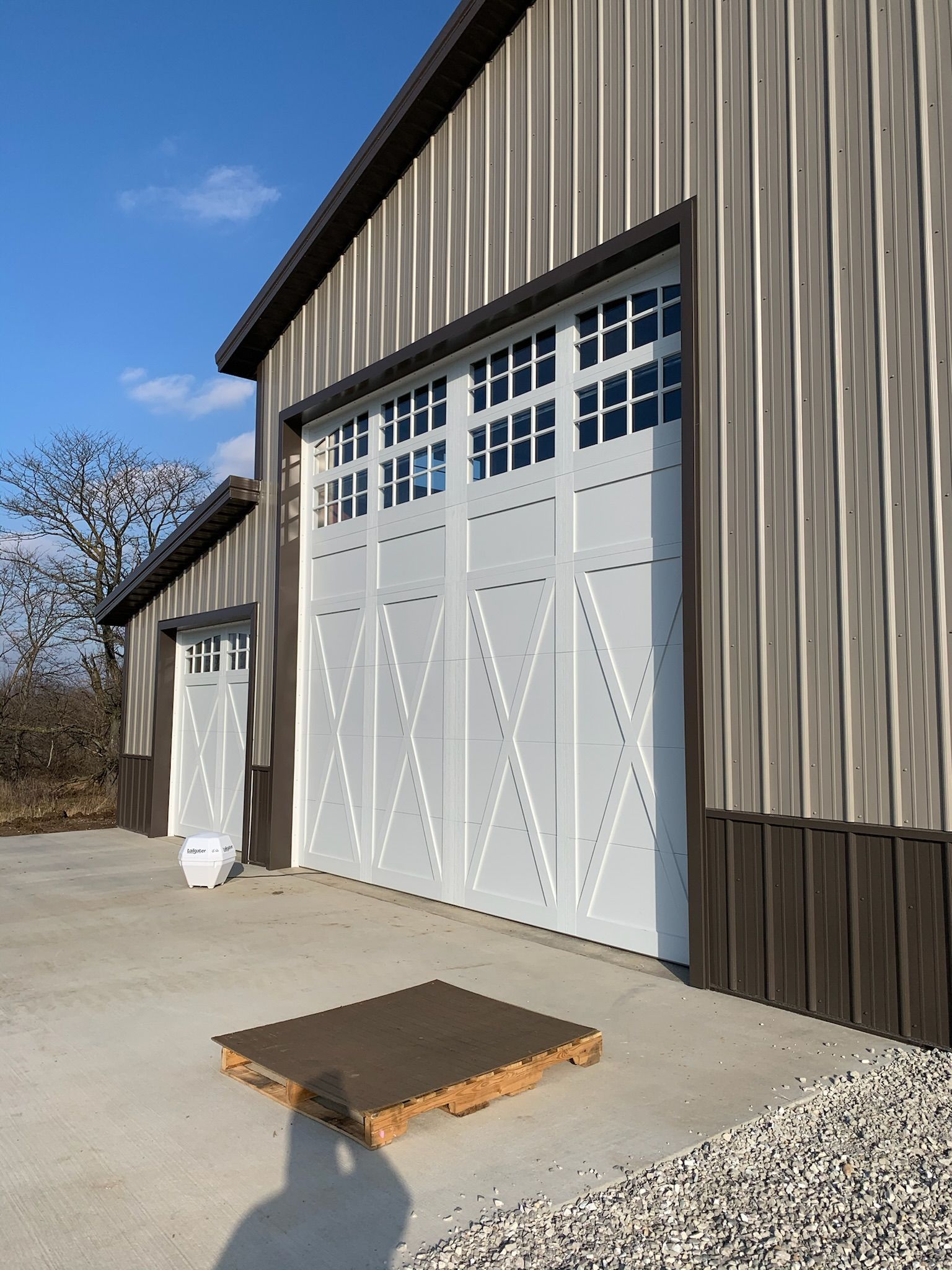 Gray metal building with a large white garage door and smaller door, set on a concrete pad.