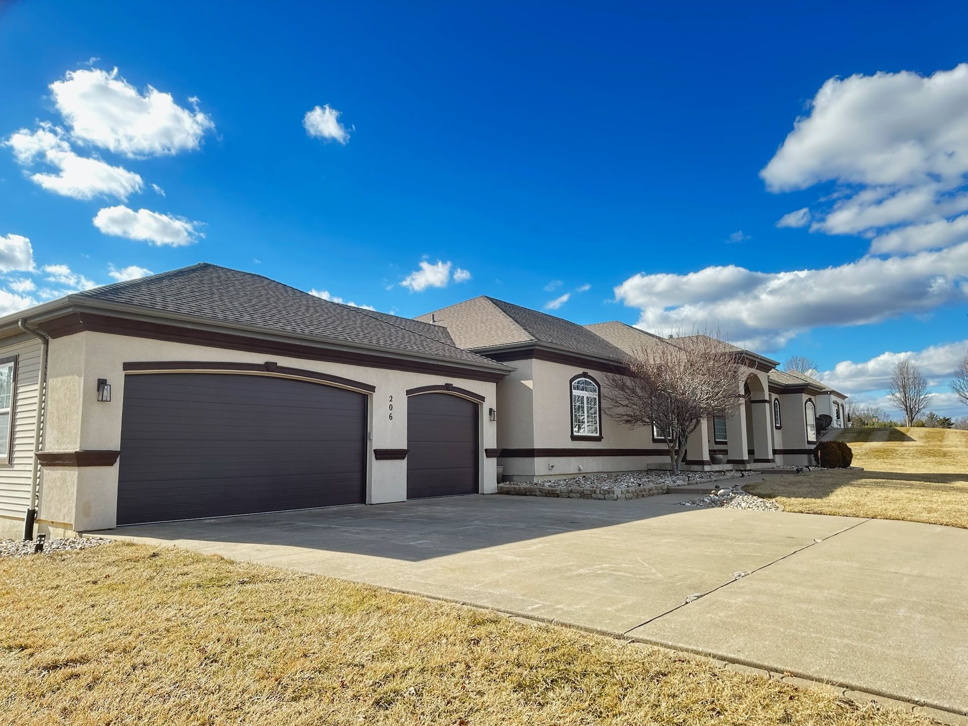 House with attached garage, stucco exterior, gray garage doors, blue sky with clouds.