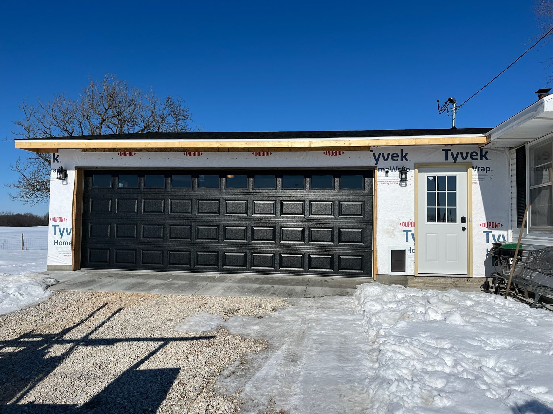 Garage with black door and white door, under construction, set in a snowy landscape.