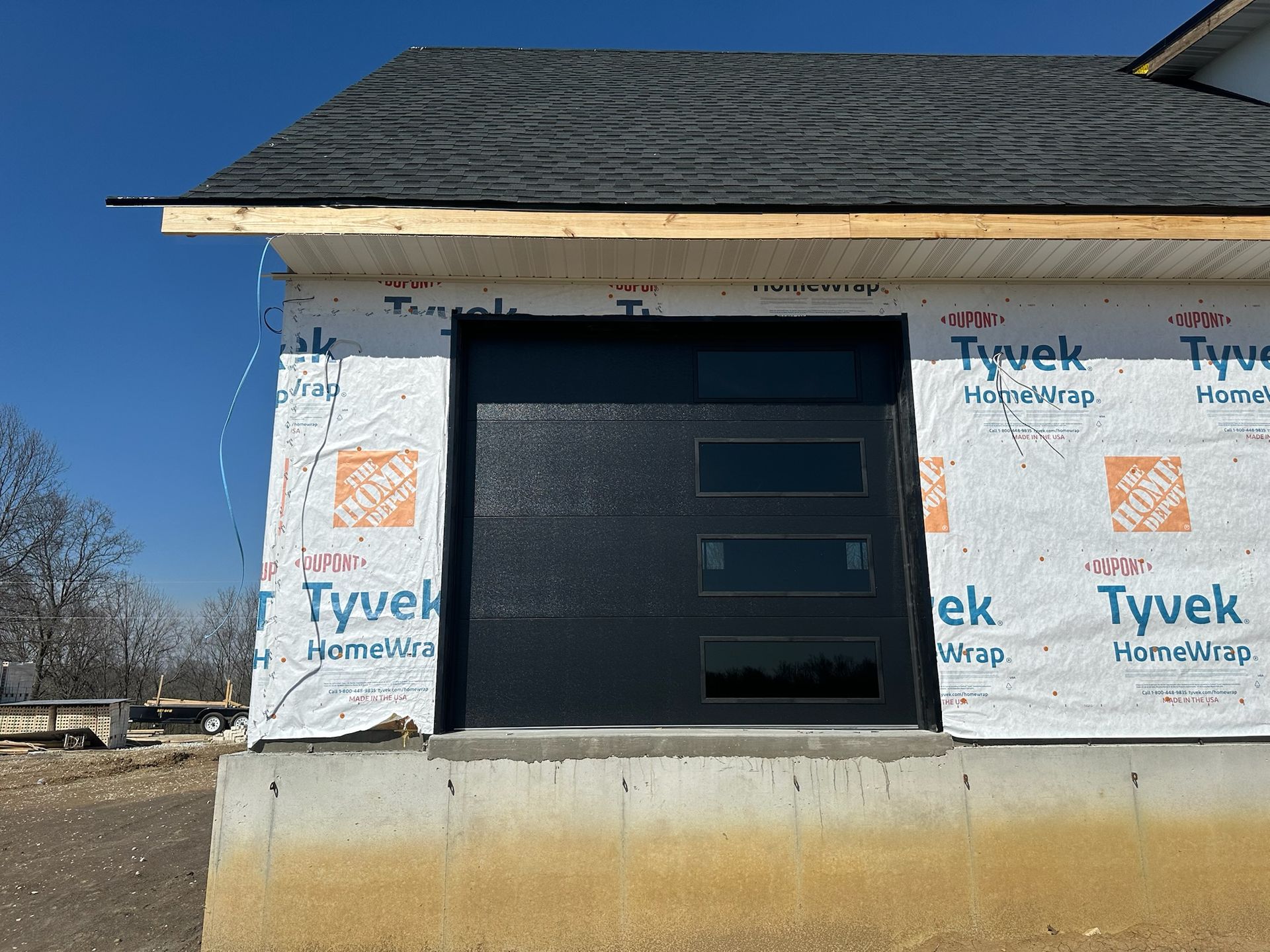 Garage door on a new home under construction, with Tyvek wrap and a dark door with windows.