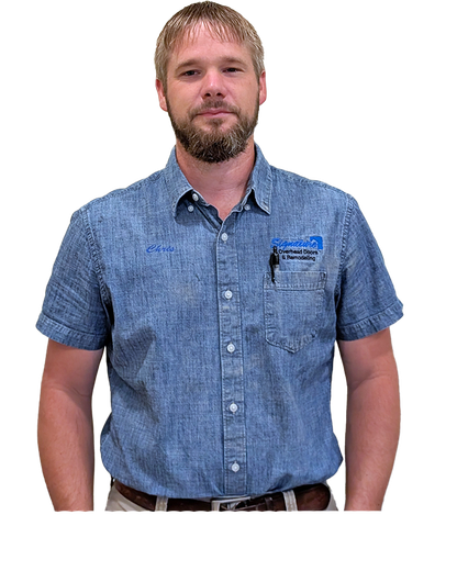 Man wearing a denim shirt, standing, with a name tag. He has a beard and is looking at the camera.
