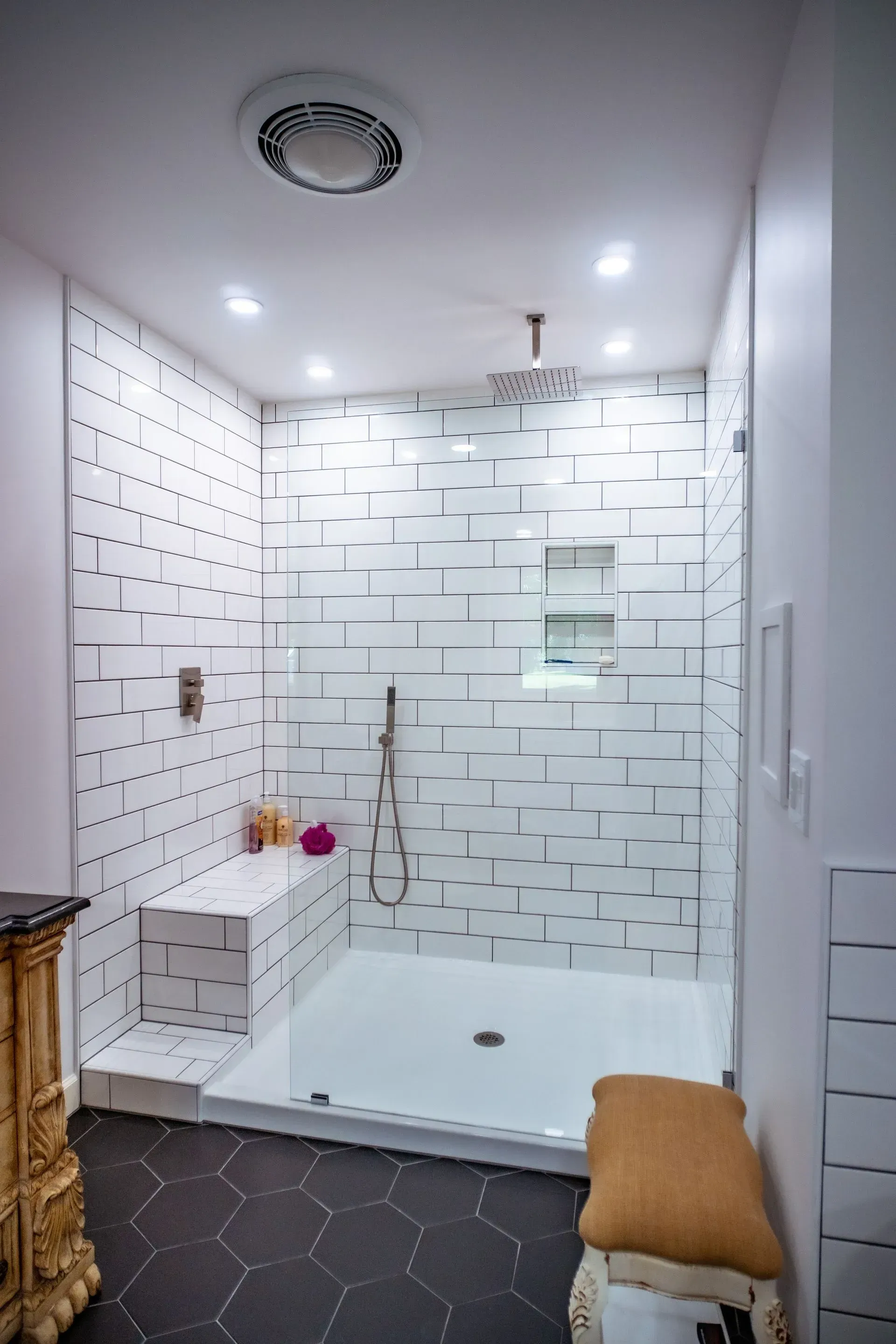 Modern white tiled shower with glass door, bench, and black hexagonal floor tiles.
