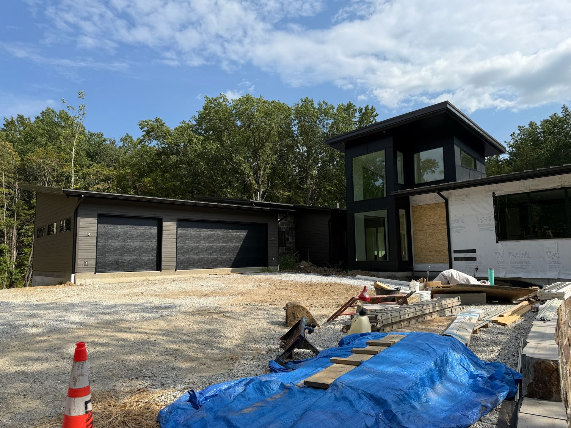 Modern house under construction with black garage doors, large windows, and gravel driveway.