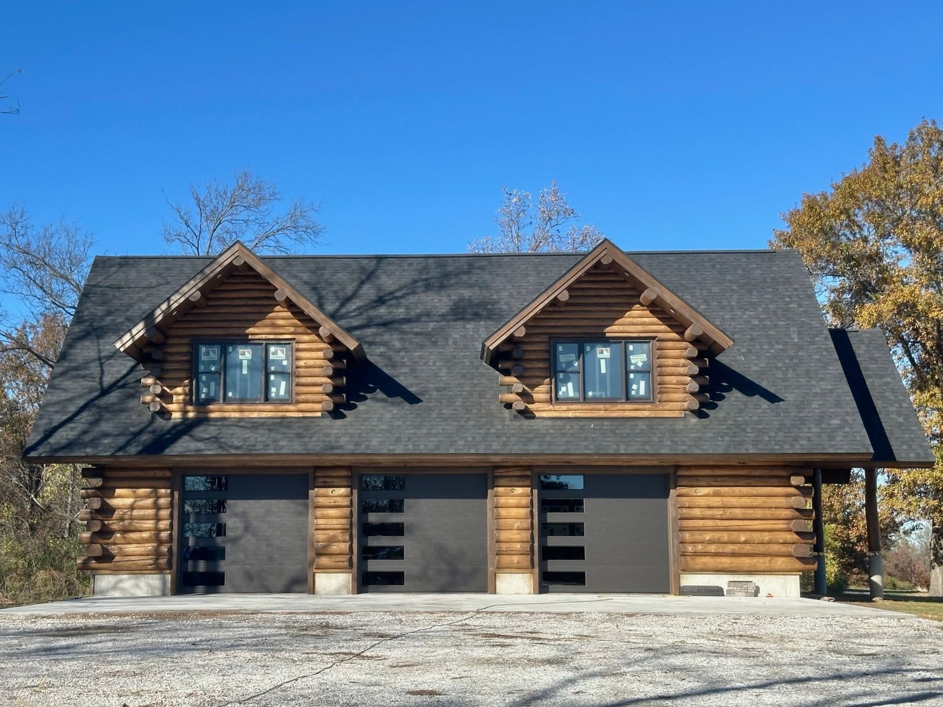 Log cabin-style two-car garage with dark gray doors and black roof under a blue sky.
