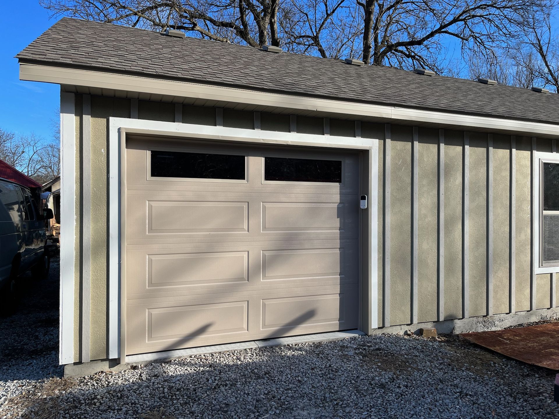 Beige garage with a tan door, trim, and light brown roof under a blue sky.