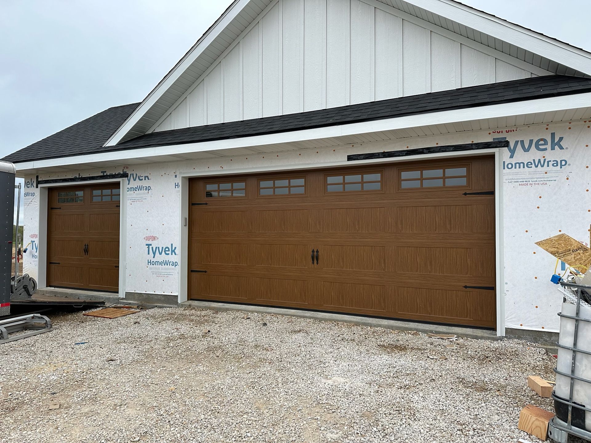 Two brown garage doors on a new construction house, with gravel driveway. White siding.