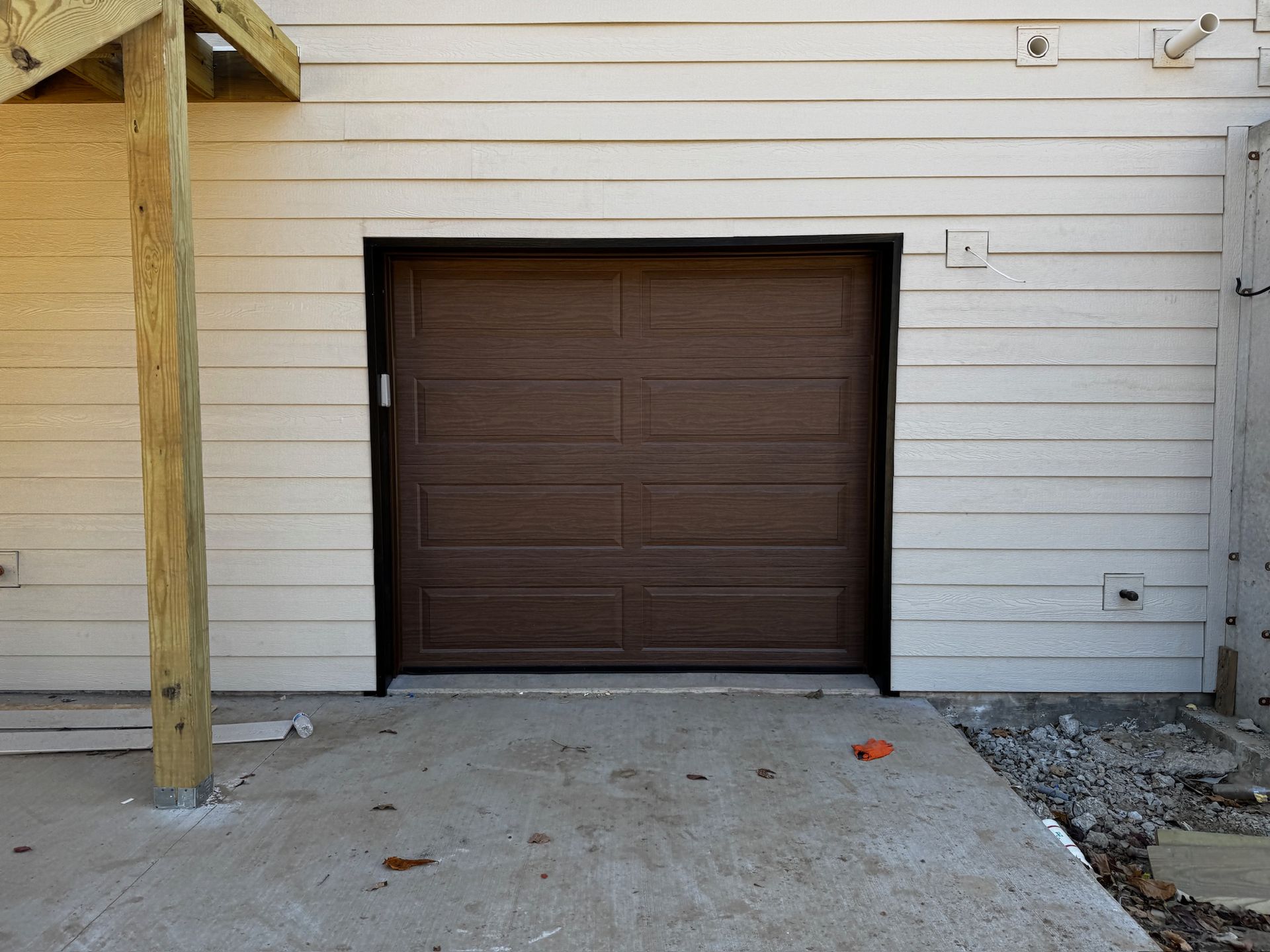 Brown garage door in a tan building facade. Concrete slab in front.